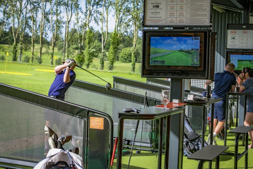 Man hitting balls on driving range showing the trackman screen