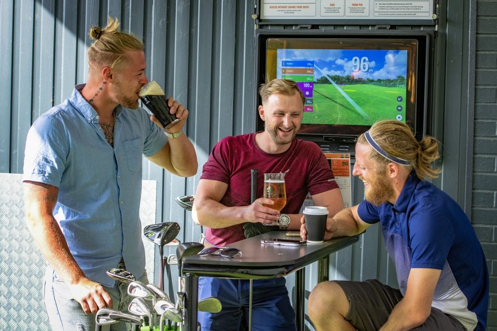 Three men socialising with a drink at the driving range in kent