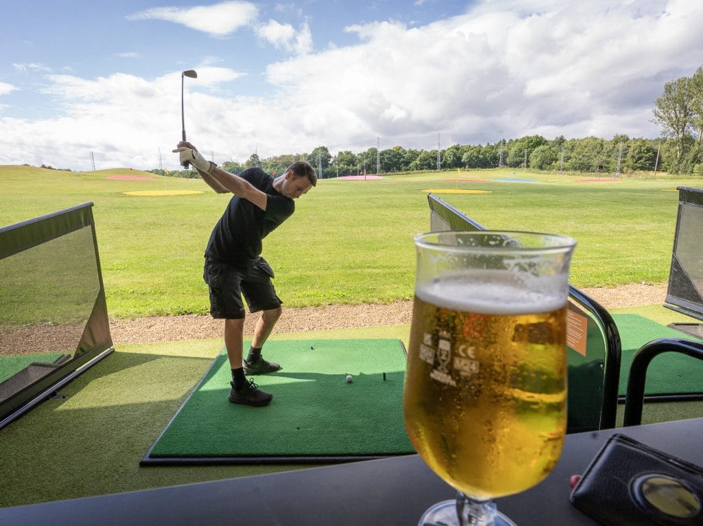 Man hitting driving range balls with pint in the foreground in kent