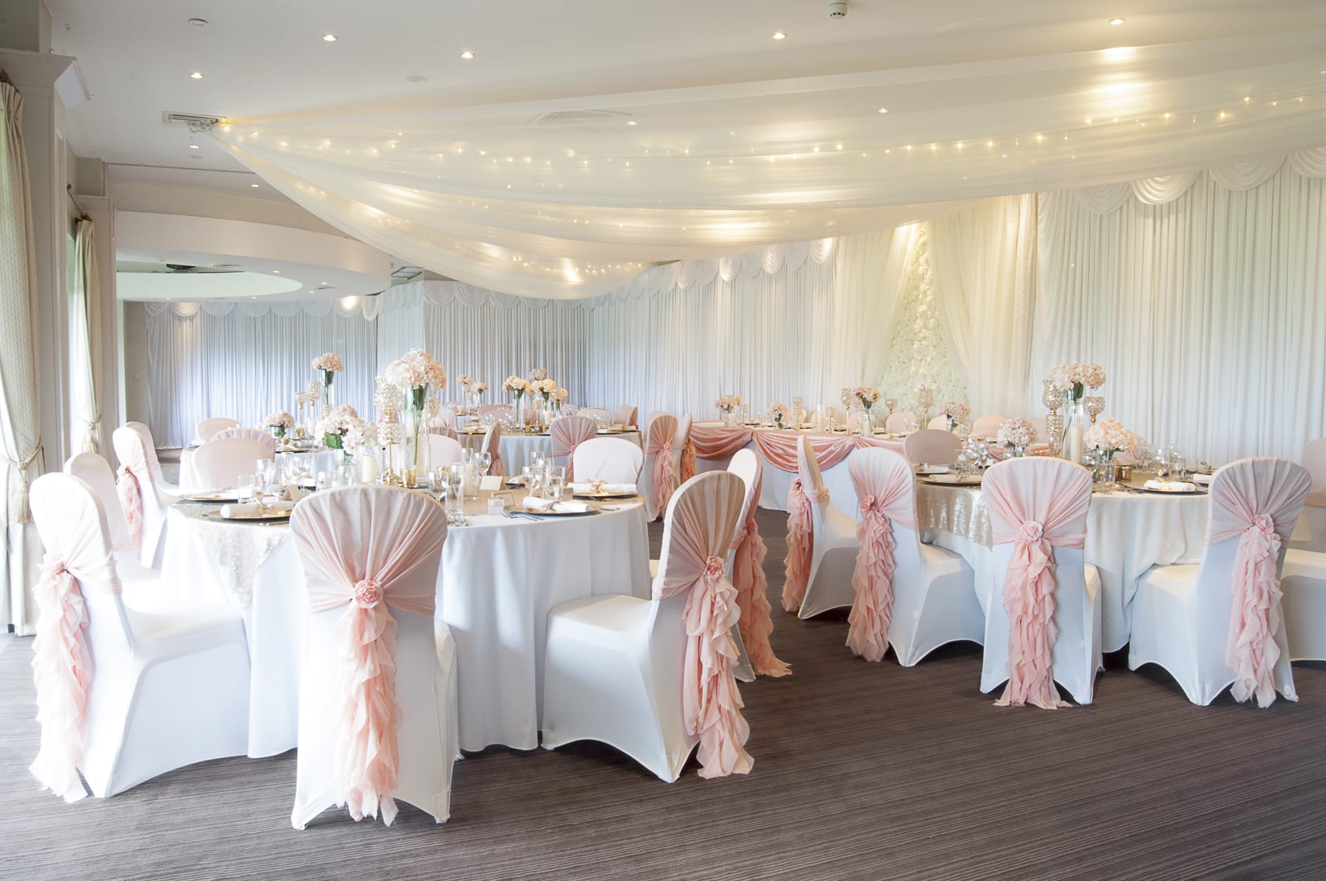 Wedding reception in dartford with a table layout with pink chair sashes and wall draping