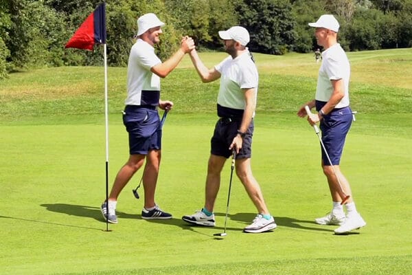 3 male golfers celebrating with each other on green at golf club in dartford