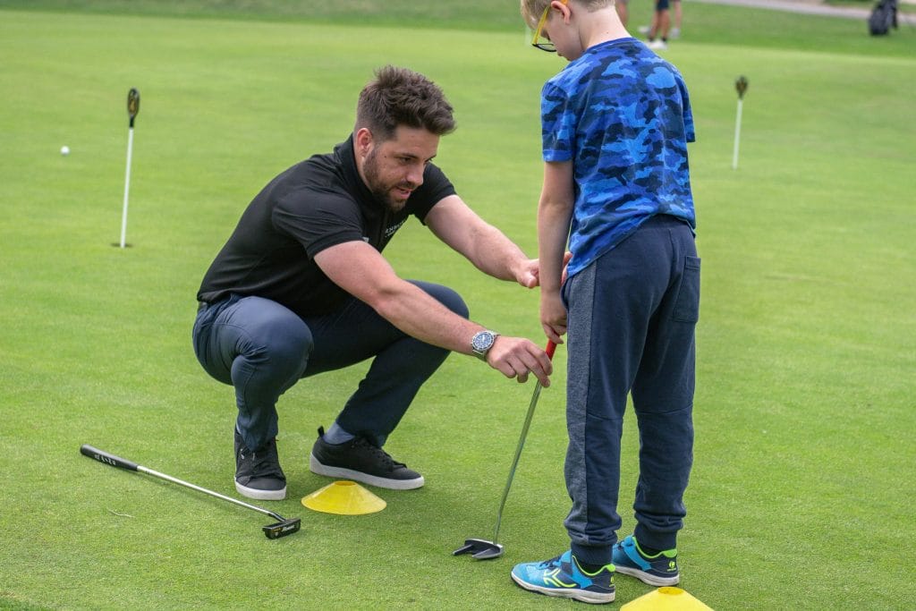 golf coach teaching junior on putting green