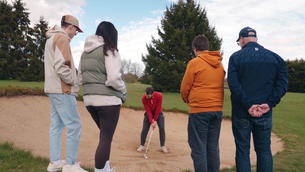 Group of learner golfers watching the coach in the bunker